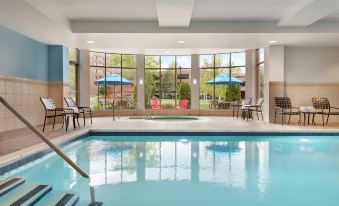 an indoor swimming pool surrounded by glass windows , providing a view of the outside world at Hilton Garden Inn Stony Brook