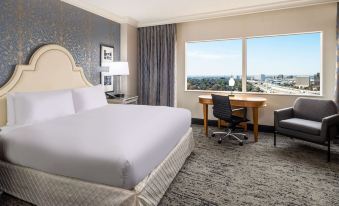 a hotel room with a bed , desk , and chair , as well as a window overlooking the city at Hilton Dallas Lincoln Centre
