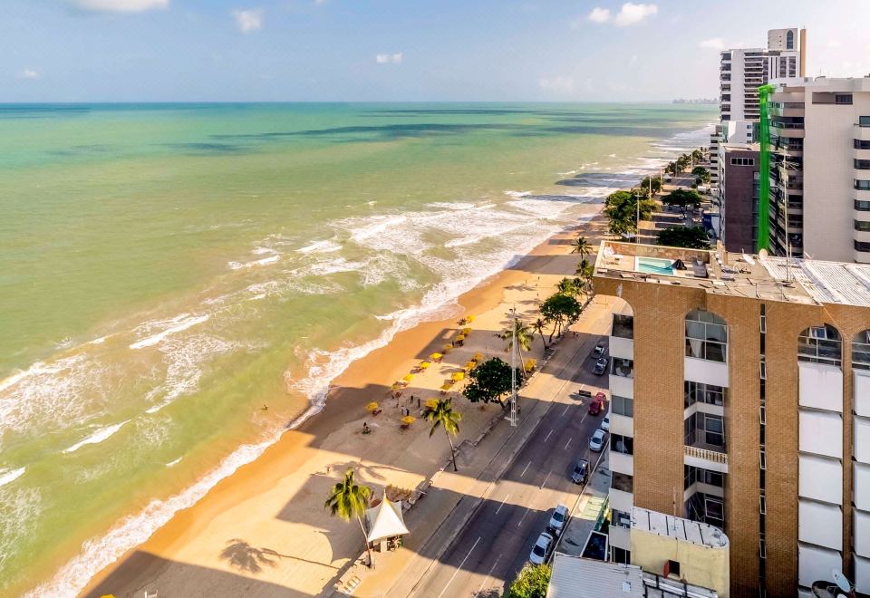 a beachfront street with a view of the ocean , buildings , and palm trees , creating a picturesque scene at Grand Mercure Recife Boa Viagem