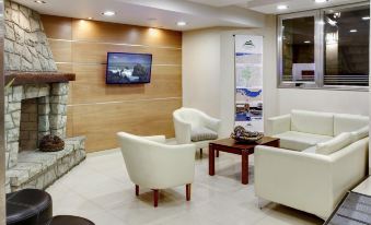 a modern office lounge area with white chairs , a fireplace , and a tv mounted on the wall at Cambria