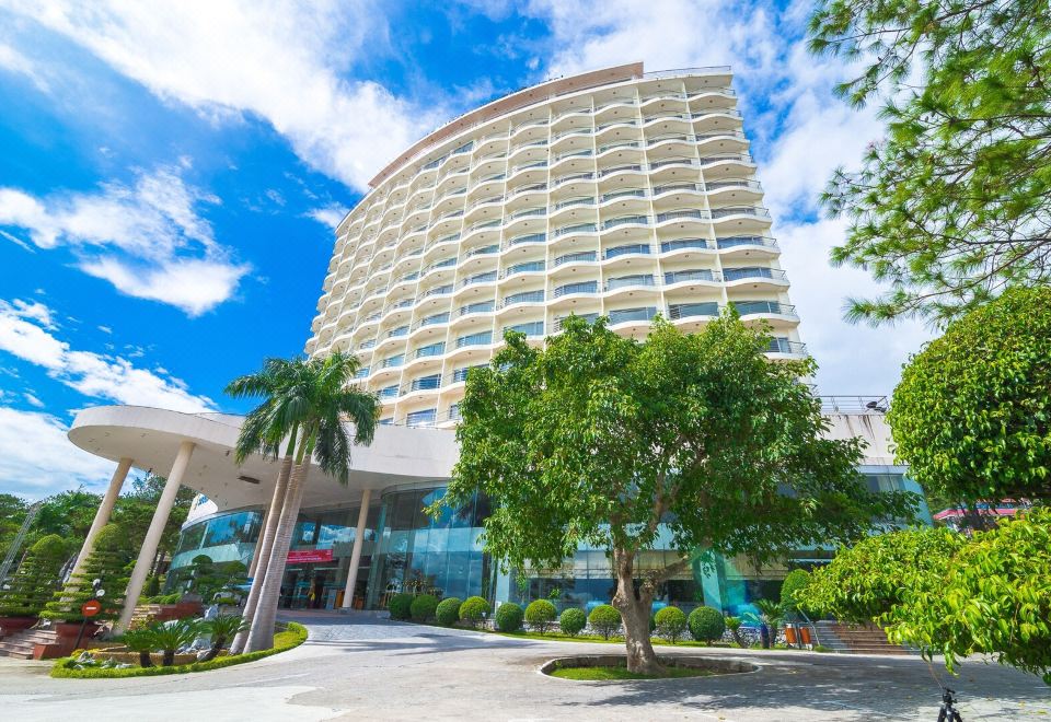 a large hotel with a curved facade and palm trees in front of it , under a blue sky at Sai Gon Ha Long Hotel
