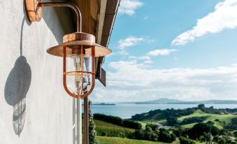a copper - colored lantern with a woven top is attached to a white wall , overlooking a serene landscape and the sea at Mudbrick Cottages