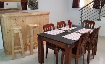 a dining room with a wooden table , four chairs , and a bar area in the background at Ibisa Hotel