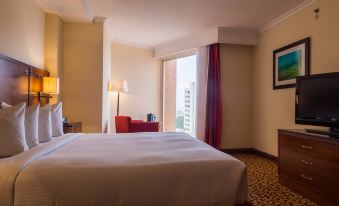 a well - lit hotel room with a white bed , red curtains , and a view of the city through the window at Venezuela Marriott Hotel Playa Grande