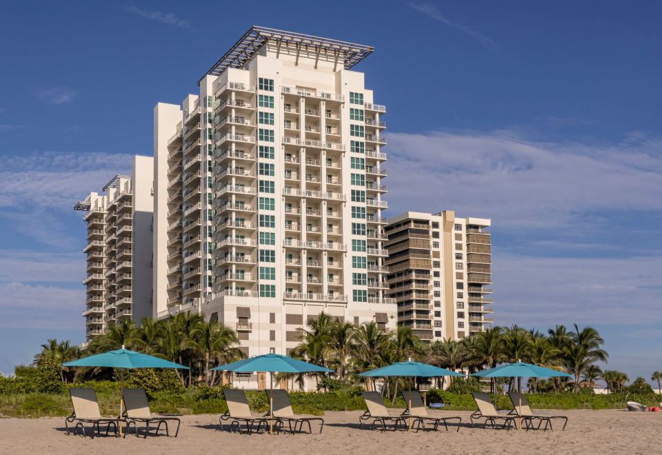 a beachfront building with multiple floors , surrounded by trees and umbrellas , under a clear blue sky at Marriott's Oceana Palms