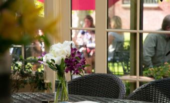 a vase of flowers is placed on a table in front of a window , with people looking at it through the window at Chamberlin Inn