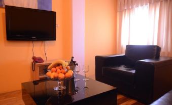 a living room with an orange wall , a black coffee table , and a flat - screen tv mounted on the wall at Alfa Hotel