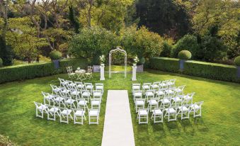 a wedding ceremony taking place in a lush green garden , with rows of white chairs set up for guests at Hilton Lake Taupo