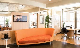 a modern office lobby with an orange couch and chairs , creating a comfortable and inviting atmosphere at Ibis Como