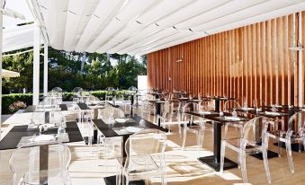 a modern outdoor dining area with white chairs and tables , under a wooden ceiling with a striped design at Globales Cala Blanca
