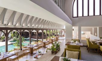 a spacious restaurant with wooden tables and chairs , a pool , and large windows overlooking the pool area at Shangri-La le Touessrok, Mauritius