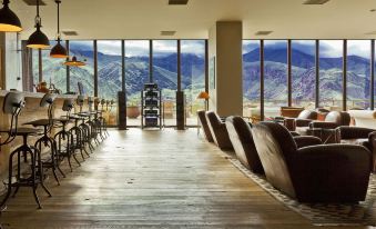 a large room with wooden floors and chairs , a dining table , and floor - to - ceiling windows overlooking a mountain range at Rooms Hotel Kazbegi