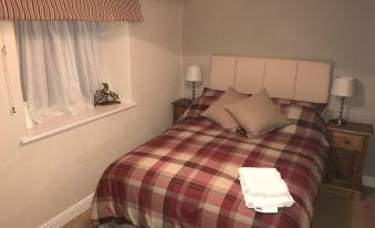 a bed with a plaid blanket and pillows is in a room next to a window at The Black Bull