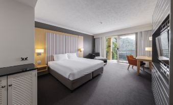 a hotel room with a large bed , a desk , and a balcony overlooking a body of water at Mercure Gold Coast Resort