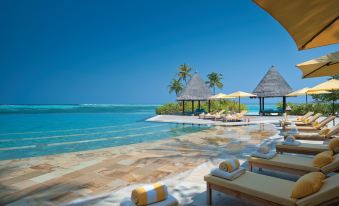 a luxurious beach resort with a swimming pool , sun loungers , and umbrellas , surrounded by palm trees and the ocean at Four Seasons Resort Maldives at Kuda Huraa