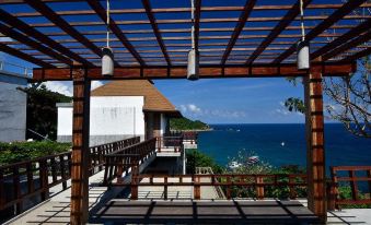 a wooden pergola overlooking the ocean , with a table and benches in the foreground and a balcony on the upper level at Sai Daeng Resort