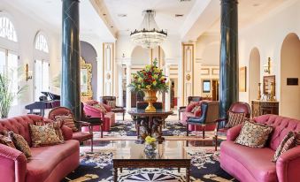 a luxurious hotel lobby with pink and purple seating arrangements , a large chandelier , and floral arrangements at Bourbon Orleans Hotel