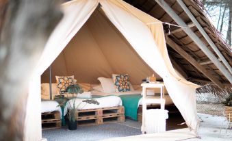 a cozy bed inside a wooden tent with pillows , surrounded by plants and a small table at Cabana Retreat - Glamping