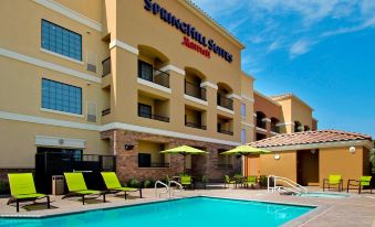 a large swimming pool with several lounge chairs and umbrellas in front of a hotel at SpringHill Suites Madera
