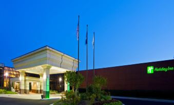 a large hotel building with a green lawn and flags in front of it at dusk at Holiday Inn Washington-Dulles International Airport, an IHG Hotel