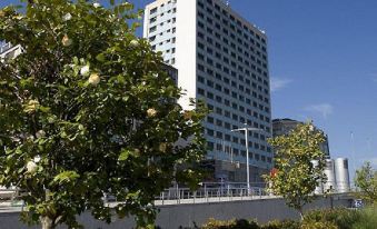 a tall white building with a blue sign is surrounded by trees and bushes in the city at Sercotel Hotel Bahia de Vigo
