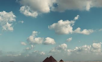 a desert landscape with three pyramids , a blue sky filled with clouds , and a large ship in the distance at Desert Moon
