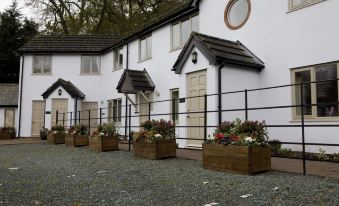 a row of houses with flower boxes and stone paving , surrounded by trees and a gravel path at Burlton Inn