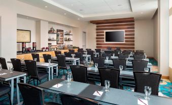 a conference room with rows of tables and chairs , a large screen on the wall , and wine glasses on each table at Residence Inn by Marriott Boston Watertown