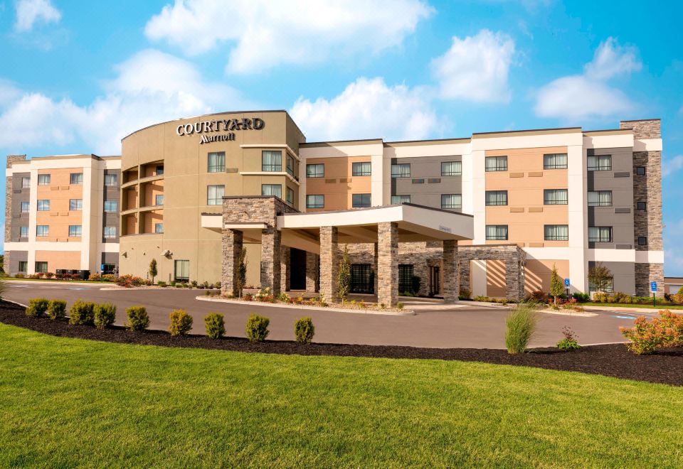 a large hotel building with multiple parking spaces and an outdoor seating area , surrounded by a grassy field at Courtyard Cleveland Elyria