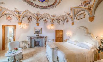 a luxurious bedroom with a large bed , white furniture , and a fireplace under an ornate ceiling at Monastero di Cortona Hotel & Spa