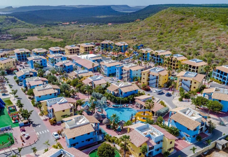 a bird 's eye view of a city with colorful buildings and a large pool surrounded by trees at Kunuku Resort All Inclusive Curacao, Trademark by Wyndham