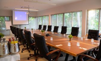 a conference room with a long wooden table , black chairs , and a projector screen , set up for a meeting at Joali Maldives