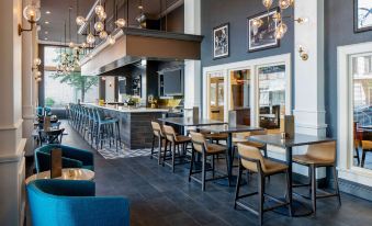 a modern restaurant with blue chairs and tables , a bar area , and hanging light fixtures at Hilton Garden Inn Jackson Downtown