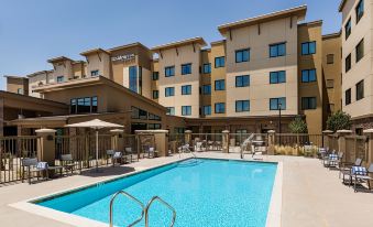 a large swimming pool with a building in the background and umbrellas around it , set against a clear blue sky at Residence Inn Riverside Moreno Valley