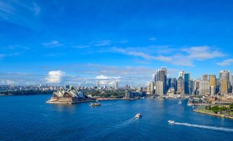 a panoramic view of the sydney opera house and city skyline , with boats on the water and clouds in the sky at 57Hotel