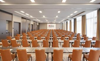 a large conference room with rows of chairs arranged in a semicircle , and a projector screen on the wall at Hilton Garden Inn Zurich Limmattal