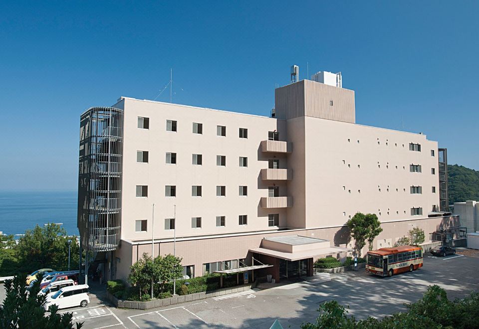 a large , beige - colored hotel building with many windows and balconies , situated in a city area surrounded by trees and cars at Kamenoi Hotel Atami Annex