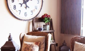 a cozy living room with two chairs , a clock on the wall , and a potted plant at Maison