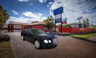 a black bentley on a driveway next to a building , with cars parked in the background at Lake Macquarie Motor Inn