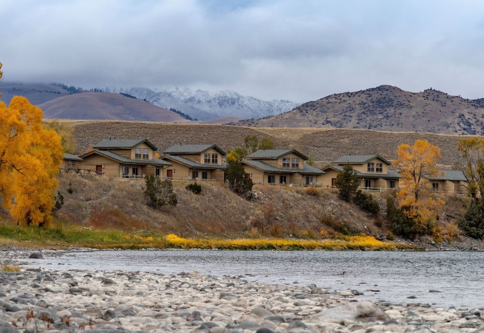 a row of small wooden houses on a hillside near a river , with mountains in the background at Yellowstone Valley Lodge, Ascend Hotel Collection