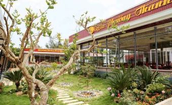 a restaurant with a large tree in front of it , surrounded by greenery and flowers at Hoang Trung Co to Hotel