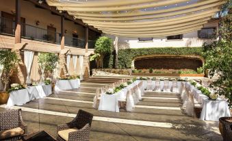 a large outdoor event space with white chairs and a stage , under a canopy of greenery at DoubleTree by Hilton Claremont