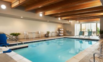 an indoor swimming pool with wooden ceiling , white walls , and a blue floor , surrounded by chairs and tables at Home2 Suites by Hilton Milwaukee Brookfield