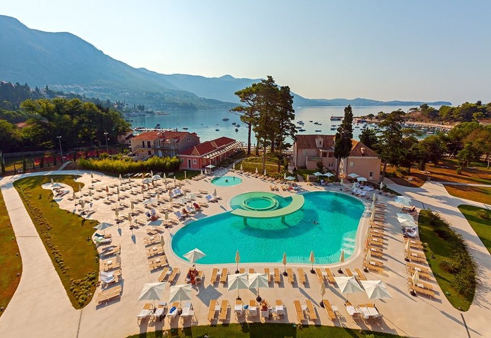a large outdoor pool surrounded by lounge chairs and umbrellas , with mountains in the background at Sheraton Dubrovnik Riviera Hotel