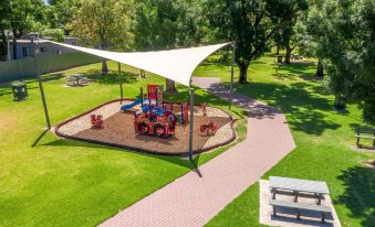a playground with a sandy area , benches , and a large white canopy in a park - like setting at Adelaide Caravan Park - Aspen Holiday Parks