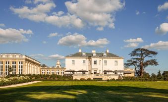 a large , white building with multiple windows and balconies is surrounded by lush greenery and umbrellas at The Langley, a Luxury Collection Hotel, Buckinghamshire