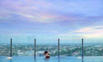 a man is standing in a swimming pool with a cityscape in the background , posing for a picture at Grand Zuri Dumai