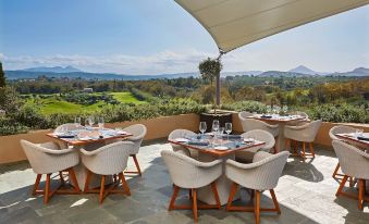 a restaurant with white chairs and tables set up on a patio overlooking a golf course at The Romanos, a Luxury Collection Resort, Costa Navarino