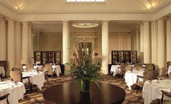 a large , elegant dining room with multiple tables set for a formal meal , featuring a large vase of flowers on one table at Macdonald Bath Spa Hotel