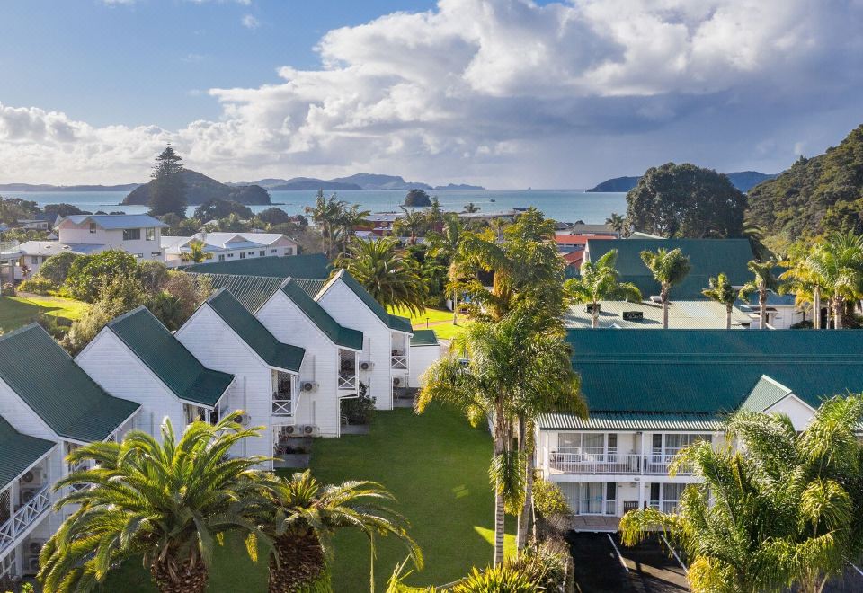 a row of white buildings with green roofs , surrounded by palm trees and overlooking the ocean at Scenic Hotel Bay of Islands